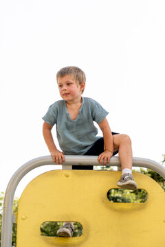 Young Boy Sits Astride Metal Playground Rail Outdoors
