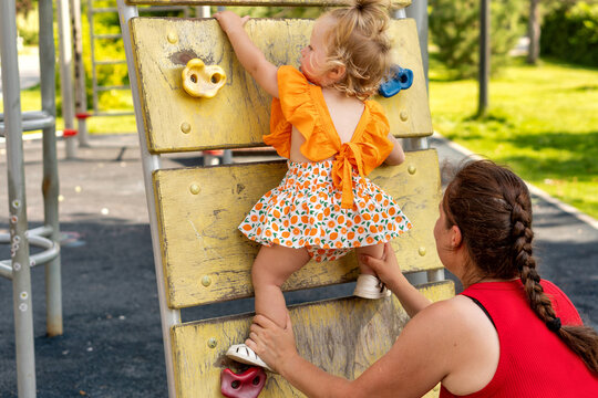 Mother Supports Toddler Climbing Outdoor Playground Wall