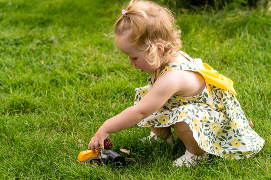 Toddler Girl Plays with Toy Truck on Grass