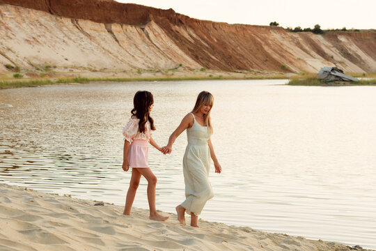 Woman And Teen Girl Walking Hand In Hand By Lake
