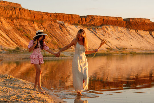 Mother And Daughter Walking Hand In Hand At Sunset