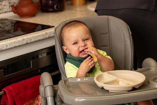 Grimacing Baby Boy Chews Spoon During Kitchen Mealtime