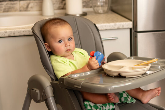 Baby Boy Holds Toy After Mealtime In Kitchen High Chair