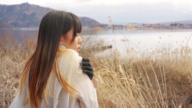 Young Asian woman tourist solo travel Mount Fuji and relaxing by  Lake Kawaguchi in Japan. Female traveler enjoy sightseeing scenic winter landscape, holiday vacation and Japanese landmark tourism