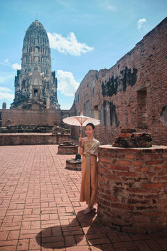Portrait of Asian teenage girl dressed in Thai traditional outfit with cheerful smile and looking at camera, holiday travel in Ayutthaya, Southeast Asia, ancient ruins heritage,  tourist destination.