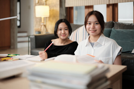 Two Asian teenage girls learning tutorials at home together, cheerful smiling, looking at camera, self-tutorial exams, preparation for school exam, Homeschooling study, knowledge education lifestyle.