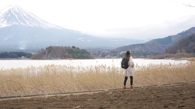 Young Asian woman tourist solo travel Mount Fuji and Lake Kawaguchi in Japan. Female traveler with backpack enjoy sightseeing scenic winter landscape, holiday vacation and Japanese landmark tourism