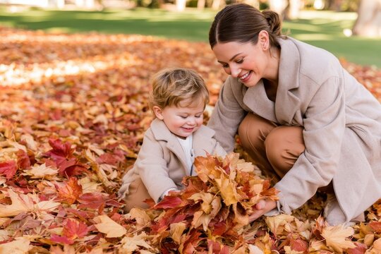 Warm family moment with mother crouching beside her small son playing in colorful autumn leaves