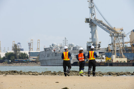 Industrial engineers inspecting cargo ship at port, wearing safety helmets and reflective vests, discussing logistics and maritime operations, teamwork in shipping and global trade industry.