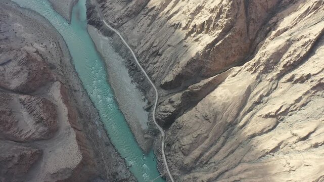 Aerial view of the Tasha Ancient Road winding through the majestic canyon and river valley in Taxkorgan, Xinjiang, China, showcasing the stunning natural landscape of the Pamir Plateau.