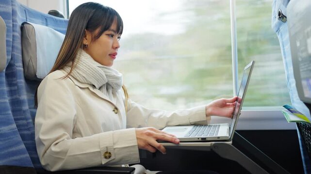 Asian businesswoman working on laptop while traveling by train, business travel, remote work and workation lifestyle. Female professional using computer during railway journey transportation commute