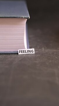 Feeling Word on White Paper Placed by Hand on Book Black Background