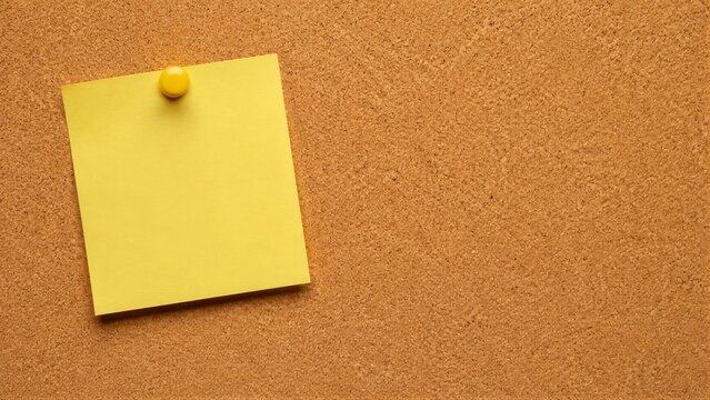 Yellow sticky note pinned on cork board notice background