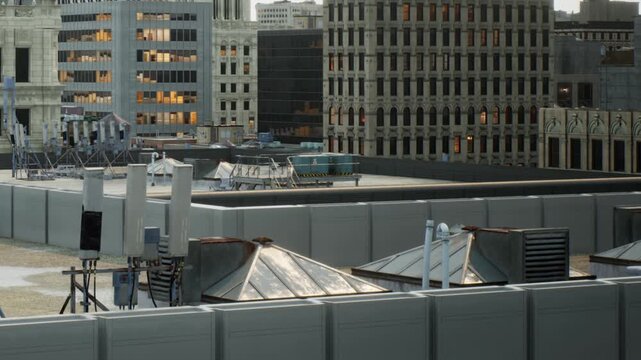 Workers are on the rooftops of buildings in a city during the day. Structures include various vents and cooling units seen near the edges of the roofs.