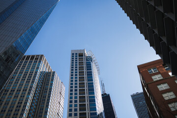 Fototapeta premium City buildings reach toward the blue sky in a downtown area during daytime with bright sunlight above