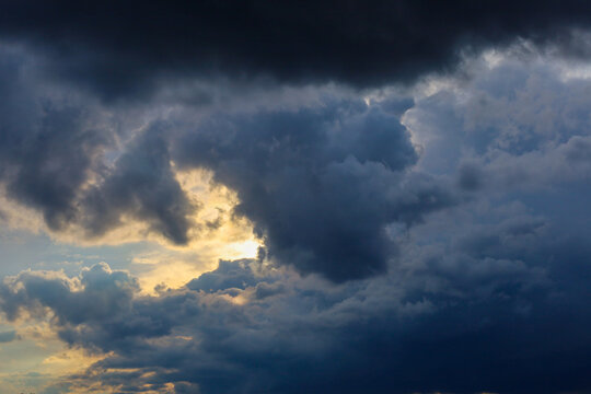 Dark storm clouds in deep blue and gray tones roll across the sky while catching a glimpse of golden sunlight. This dramatic sky landscape highlights the vivid contrast of light and shadow right befor