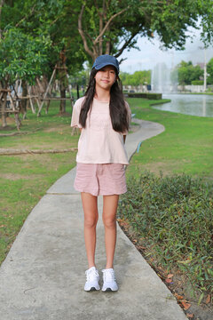 Portrait of lovely young Asian girl wearing casual and cap hat is standing, posing on a pathway in the park.