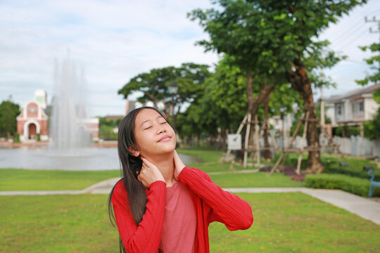 A beautiful young Asian girl in a red cardigan stretches her neck while standing peacefully in a park.