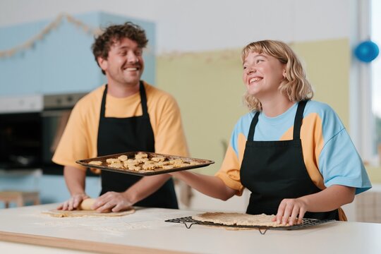 Floating tray of baked biscuits in a bright kitchen, featuring a surprised couple and dusting of flour for baking and home appliance ads, copy space