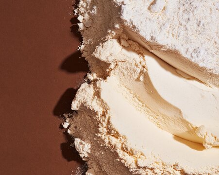 Loose white flour and icing sugar drifts on a dark brown surface, showing a powdery crystalline texture for food backgrounds and packaging design