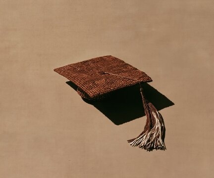 Mortarboard graduation cap with woven kente pattern and beadwork, featuring a textured finish on a warm taupe background for cultural craft layouts