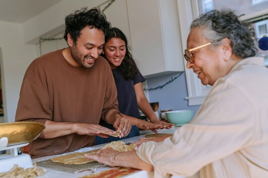 South Asian family shaping dough together in a kitchen, a natural multigenerational moment of holiday baking for lifestyle and food content