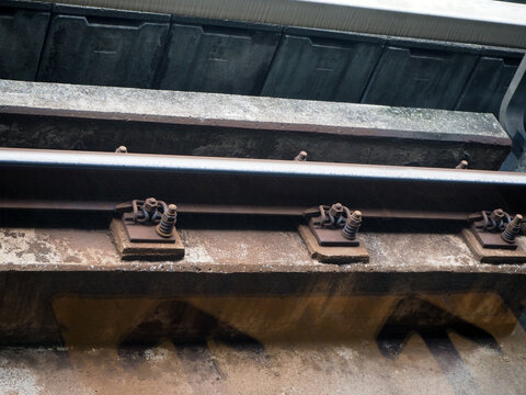 Close-up of rusty train tracks and fasteners, highlighting the weathered industrial infrastructure. The image shows the texture and detail of the railway components, suggesting a journey or transit