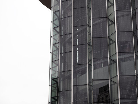 A close-up of a modern glass building with geometric patterns and a spiral staircase visible inside. The architecture is sleek and contemporary.