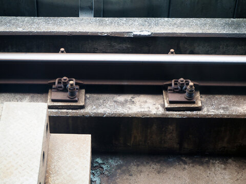 Close-up of train tracks with industrial metal components and concrete beam