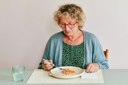 Senior woman using adaptive tableware to eat a meal in a quiet day room, featuring a plate guard and weighted fork for care marketing