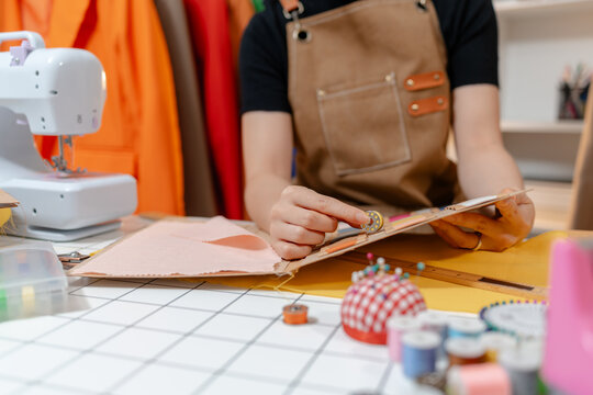 Professional fashion designer selecting fabric swatches, thread colors and sewing supplies in a modern studio. Creative textile design, apparel development and garment production.