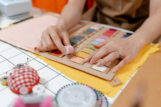 Professional fashion designer measuring fabric, selecting colors and preparing sewing equipment in a modern studio. Creative garment production, textile craftsmanship and apparel design.