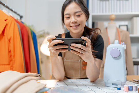 Professional fashion designer using a smartphone while managing a sewing studio and organizing tailoring supplies. Creative apparel production, small business and handmade craftsmanship.