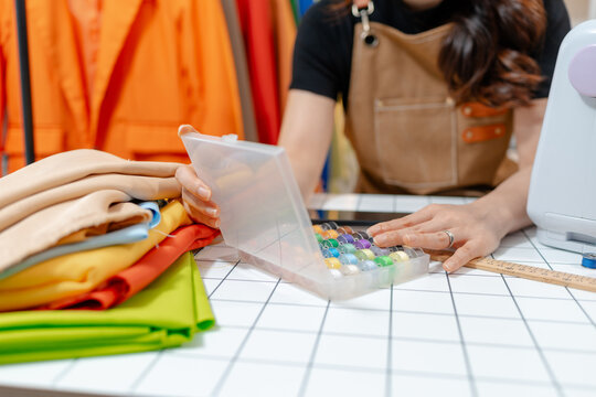 Professional fashion designer using a smartphone while managing a sewing studio and organizing tailoring supplies. Creative apparel production, small business and handmade craftsmanship.