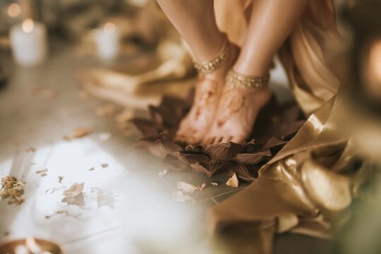 Decorated feet of a Hindu goddess statue resting on a brown lotus, featuring glowing gold fabric and ornate anklets for Diwali and Indian heritage