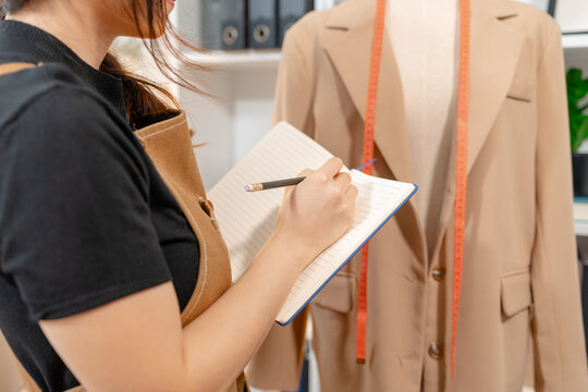 Fashion designer inspecting garment quality, measuring blazer fit and recording design details in a professional fashion studio. Apparel development, clothing quality control and textile craftsmanship