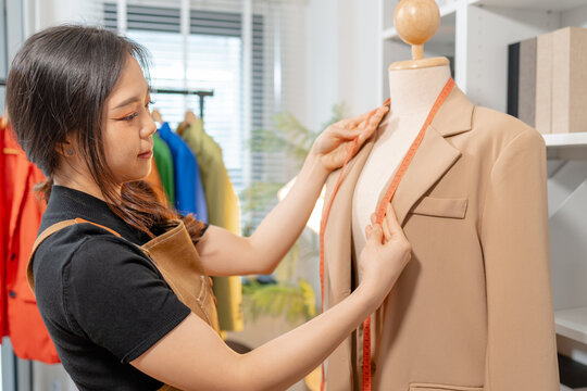 Fashion designer inspecting garment quality, measuring blazer fit and recording design details in a professional fashion studio. Apparel development, clothing quality control and textile craftsmanship