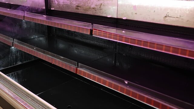 Empty refrigerated shelves and display cases in a grocery store or supermarket. Retail supply chain crisis, food shortage, out of stock, economic issues and empty market concept.