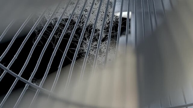 Blurred fan blades move behind a dusty metal grill in a close interior view.