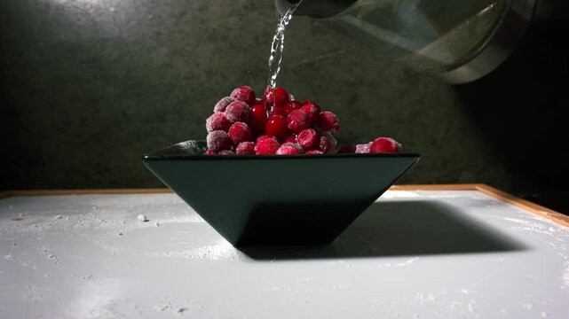 Pouring hot water on frozen bowl of cranberries 4k close up slow motion shot
