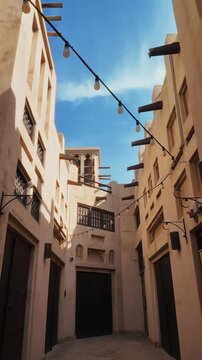 Cinematic reveal opens on a traditional Arabian-themed souk street in Dubai, then camera pushes in. Sandstone walls, wooden doors, wind tower, mashrabiya, string lights.