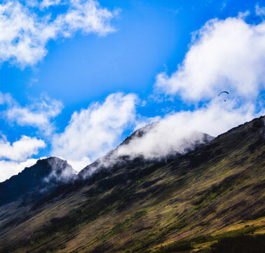 Dramatic cloudscape over the Chugach Mountains in Anchorage, Alaska, a summer morning landscape view from Glen Alps Hiking Trail, with a hanglider flying in the air