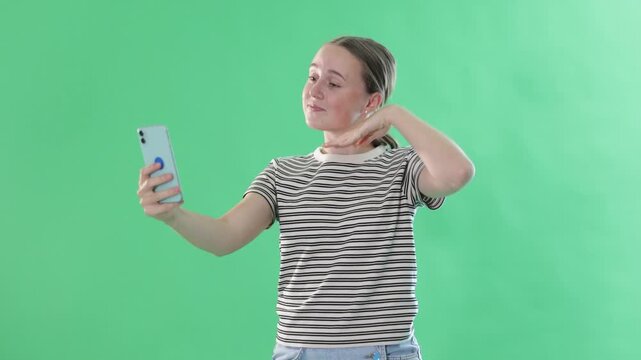Happy teenage girl in denim skirt takes selfie on a smartphone on a green background. Chroma key compositing. High quality 4k footage