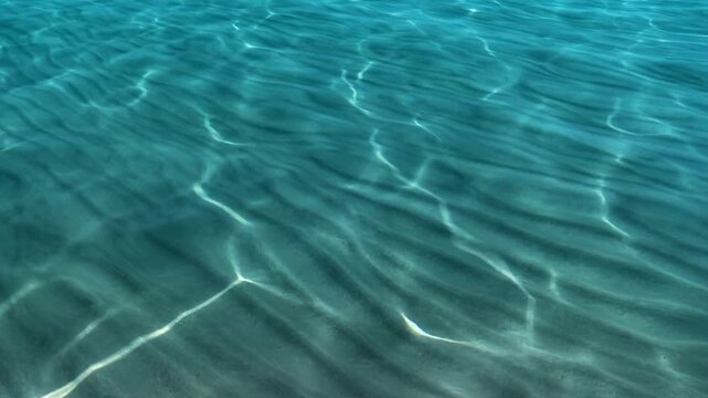 Clear azure ocean water light patterns ripples sandy bottom textures bright sun reflections.