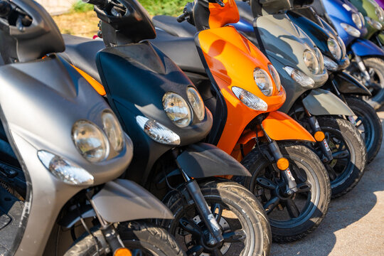 Colorful motor scooters parked in a row on a sunny street, representing sustainable transportation and a convenient way to explore Mediterranean islands during summer vacations.