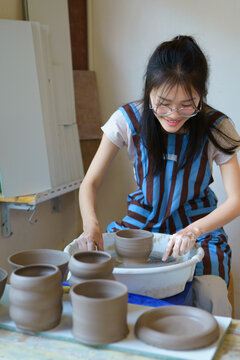 asian female ceramic artist wearing apron cutting clay bowl from pottery wheel using string, traditional handmade pottery process in creative studio with focus on craft and artistic lifestyle