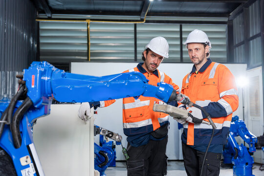 Team of engineers programming robotic arm in manufacturing plant, Technicians operating automated robot machine with controller, Workers collaborating on robotics automation project in factory