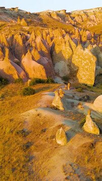 Vertical video. Goreme, Nevsehir, Turkey. Devrent Valley fairy chimney formations, aerial panoramic view at golden hour sunset over eroded volcanic tuff landscape. Aerial View. Rich colors