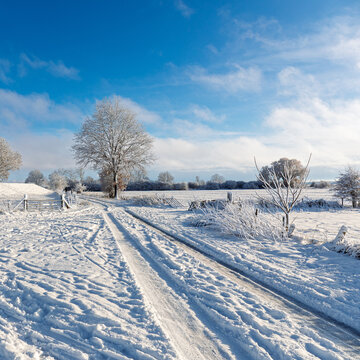 Snow-covered country road with tyre tracks in winter