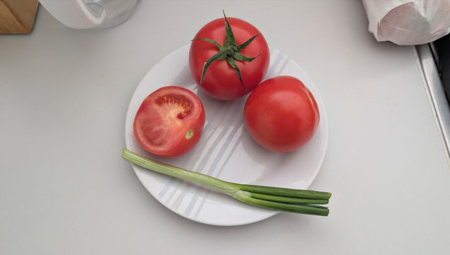 Fresh tomatoes and green onions on a white plate prepared for cooking in a kitchen
